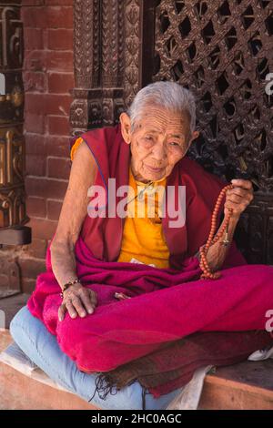 Une vieille religieuse bouddhiste avec ses perles de rossary mala assis par le Boudhanath Stupa, Katmandou, Népal. Banque D'Images