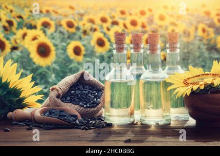 Trois bouteilles d'huile de tournesol et sac de graines de tournesol noires, magnifique champ de tournesol jaune sur fond. Banque D'Images