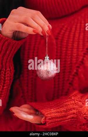Les mains des femmes dans un chandail d'hiver tricoté tenant une boule de Noël rose étincelante.Détails de la nouvelle année et atmosphère magique Banque D'Images