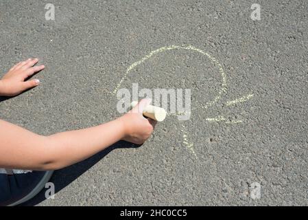 Main des enfants avec de la craie colorée, puise sur l'asphalte.Art de la rue main d'un enfant en gros plan. Banque D'Images