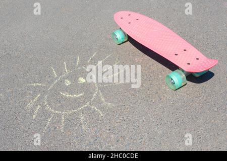 Dessiner le soleil sur l'asphalte et le skateboard en gros plan. Banque D'Images