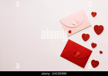Enveloppes décoratives rouges et roses avec fermeture symbolisant l'amour sur un fond brillant argenté, coeurs paillettes rouges dispersés, lieu pour des souhaits ou l'amour Banque D'Images