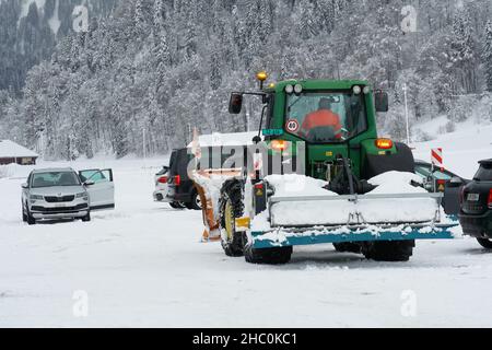 Tracteur lourd avec lame de bouteur arrière dans le parking avec voitures dans la station de ski de fond en Suisse. Banque D'Images