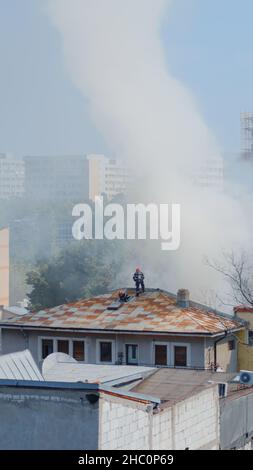 Pompiers sur le toit de la maison en feu essayant d'éteindre des flammes.Équipe de pompiers du service de lutte contre les incendies avec camion et équipement mettant le feu sur le bâtiment avec de l'eau. Banque D'Images