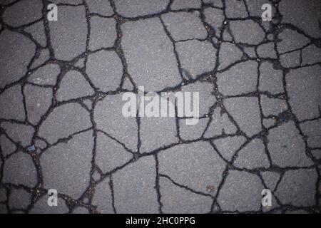 Vue rapprochée de la route asphaltée fissurée dans les fissures humides Banque D'Images