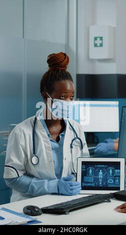 Médecin tenant un comprimé avec analyse du corps humain pour une visite de contrôle avec le patient, portant des masques contre l'épidémie de covid 19.Illustration du squelette pour le soin de l'ostéopathie. Banque D'Images