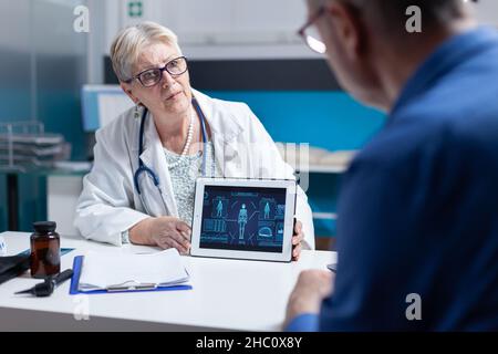 Médecin expliquant l'analyse du corps humain sur un comprimé au patient atteint d'une maladie lors de la visite de contrôle.Femme médecin et homme parlant de diagnostic avec l'illustration de l'anatomie sur l'appareil numérique. Banque D'Images