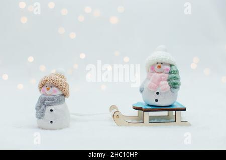 Figurines décoratives sur le thème de Noël.Deux statuettes d'un bonhomme de neige dans un chapeau tricoté sur le traîneau.Décoration festive, lumières bokeh chaleureuses Banque D'Images