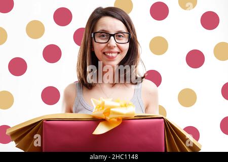 Une femme souriante et heureuse tenant un grand cadeau de Noël ou un cadeau sur un fond de pois marrons et or assorti sur fond blanc dans un conc de vacances de saison Banque D'Images