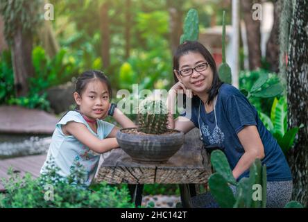 Portrait asiatique d'âge moyen mère et fille posant à une table en bois dans un beau jardin botanique, masques de visage sont suspendus sur des cols, coudes sur la table Banque D'Images