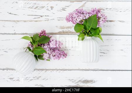 composition ressort décorative de deux mini vases en céramique blanche avec branches de lilas pourpre sur une table en bois blanc.Design original et plat Banque D'Images