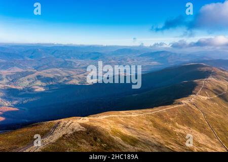 De longues allées étroites longeant la crête de haute montagne sous des nuages blancs moelleux flottant sur le ciel bleu sur une vue aérienne de jour ensoleillé Banque D'Images