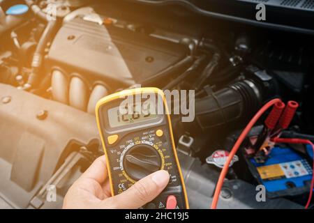 À la main d'un mécanicien, utiliser un multimètre-voltmètre pour vérifier le niveau de tension dans une batterie de voiture. Banque D'Images