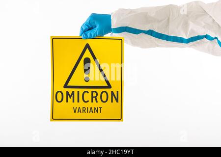 Détail d'un bras d'une infirmière médicale portant un EPI et des gants en latex avec un signe jaune avec un symbole de danger qui se lit comme suit : 'VARIANT OMICRON'.Coronavirus, Banque D'Images