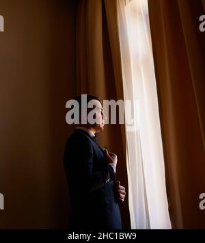 jeune homme dans une chemise blanche attache des boutons de manchette sur les manches près de la fenêtre. portrait d'affaires.Le marié va rencontrer la mariée.Mariage. Homme d'affaires Banque D'Images