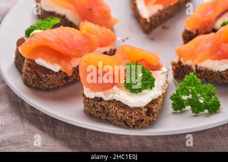 Mini sandwiches avec du saumon, du fromage caillé, du persil et du pain de seigle sous forme de coeurs.Saint-Valentin cuisine créative maison.J'adore le design du petit déjeuner.Séle Banque D'Images