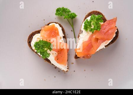 Mini sandwiches avec du saumon, du fromage caillé, du persil et du pain de seigle sous forme de coeurs.Saint-Valentin cuisine créative maison.J'adore le design du petit déjeuner.Séle Banque D'Images