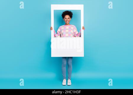 Vue sur toute la longueur du corps de fille gaie attrayante tenant le cadre d'image isolé sur fond bleu vif Banque D'Images