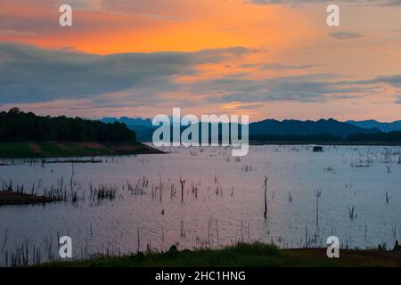 Paysage d'un lac tropical au crépuscule, une maison flottante et un filet de pêche traditionnel sur un lac, des montagnes et le ciel de coucher du soleil.Thaïlande. Banque D'Images