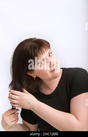 Portrait de la jeune femme avec des cheveux naturels foncés isolés sur fond blanc.Fille corrige ses cheveux.Fille peignant ses cheveux. Banque D'Images