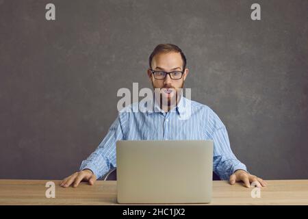 L'homme assis à la table avec un ordinateur portable est très choqué par ce qu'il a vu à l'écran. Banque D'Images