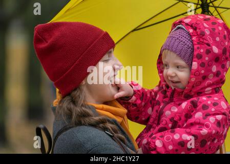 Portrait de mère et de bébé sous un parapluie jaune dans le parc.Maman et petite fille qui se berce Banque D'Images