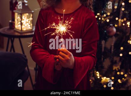 Adorable fille enfant tenant une bougie parfumée dans les mains dans la maison salon, décoré arbre de Noël sur fond, pièce sombre, éclairé par bougie parfumée.Heureux Banque D'Images