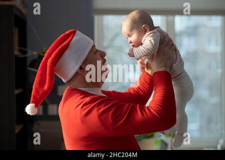 Grand-père caucasien en chapeau rouge jouant avec la petite-fille à la maison selebrating Noël Banque D'Images