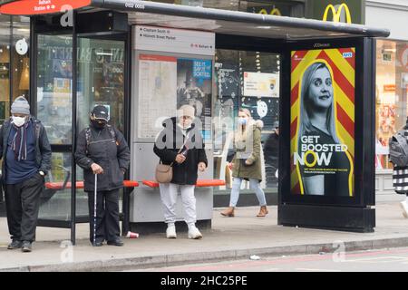 Londres, Royaume-Uni, 23 décembre 2021 : les gens font la queue à un arrêt de bus à Balham, portant déjà un masque facial désormais obligatoire pour les passagers des transports en commun.Dans les deux derniers jours de shopping avant Noël beaucoup de gens sont dehors et au sujet d'acheter des provisions et des cadeaux.Aucune nouvelle réglementation n'a été introduite en Angleterre malgré un nombre très élevé d'affaires omicron, mais on s'attend à ce qu'elle soit peu après Noël.Anna Watson/Alay Live News Banque D'Images