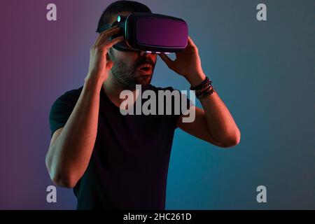 Jeune homme en lunettes VR excités interagir avec la réalité virtuelle dans la lumière de couleur néon, la technologie future, le jeu vidéo d'éducation Banque D'Images