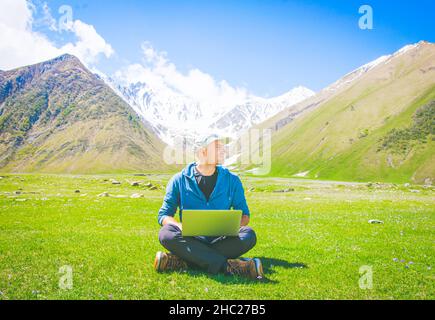 Image positive et éclatante d'un homme assis dans des vêtements décontractés sur l'herbe et regardant à droite.Idées et travail en ligne dans le monde post-pandémique. Banque D'Images