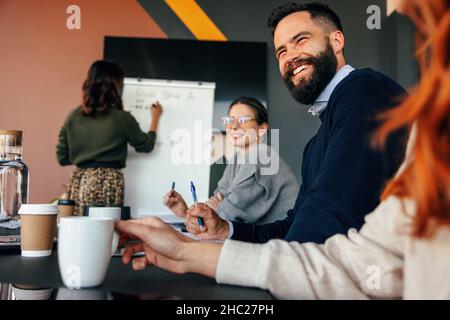 Des hommes d'affaires souriants lors d'une réunion de conseil.Groupe d'hommes d'affaires divers assistant à une présentation dans un bureau moderne.Entrée jeune Banque D'Images