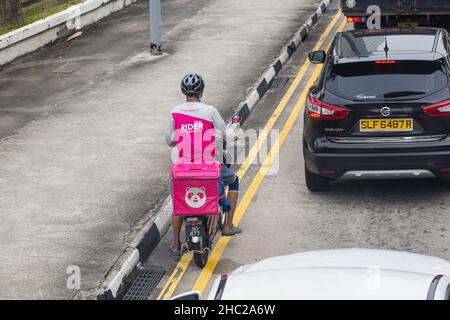 Un pilote de livraison de nourriture avec un casque de sécurité est à bord de son vélo électrique pour faire sa prochaine livraison de nourriture de client. Singapour. Banque D'Images