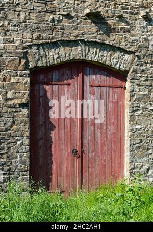 Des portes peintes en rouge forment l'entrée d'une grange traditionnelle construite sur des estons dans les Yorkshire Dales Banque D'Images