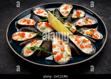 Moules cuites au four avec du fromage, du saumon, du citron et des herbes sur fond sombre Banque D'Images