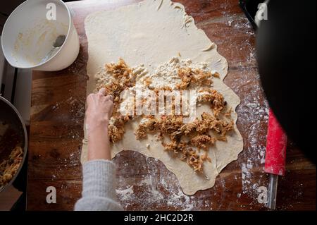 Vue de dessus d'une femme remplissant une pâte de pâte de vegan roulée avec le remplissage de raisins secs de pomme sur une table à manger maison pour faire un strudel traditionnel. Banque D'Images