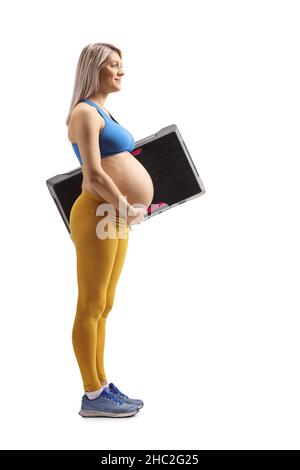 Prise de vue sur toute la longueur d'une femme enceinte en vêtements de sport tenant une plate-forme aérobie à pas isolée sur fond blanc Banque D'Images