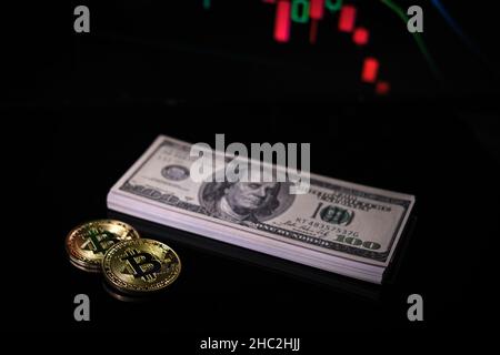 2 pièces de bitcoin sont situées à côté de la pile de billets et en arrière-plan se trouve un tableau de bitcoin tombant Banque D'Images