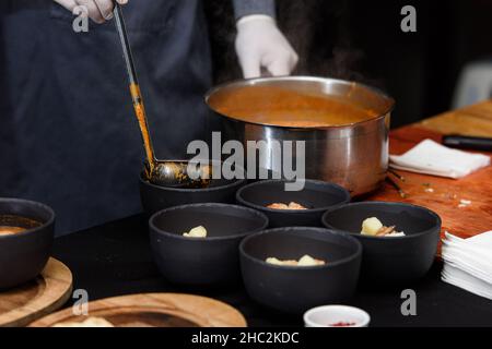 Processus de cuisson de la soupe Suquet de Peix aux pommes de terre, aux herbes et au poisson avec ajout de picada gros plan dans une casserole sur la table. Banque D'Images