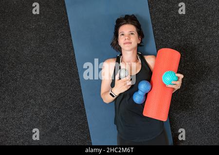 Jeune fille athlétique se trouve sur un tapis de yoga avec divers rouleaux myofascial.Equipement pour MFR.Version myofasciale.Vue de dessus. Banque D'Images