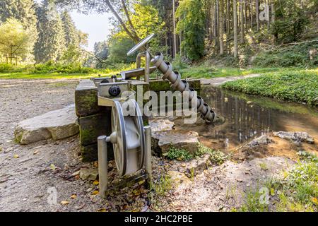 Secousse d'eau pour tirer l'eau d'un étang à côté d'une route de terre avec de nombreux arbres feuillus en arrière-plan, jour d'été ensoleillé sur le sentier Mullerthal, Luxemb Banque D'Images