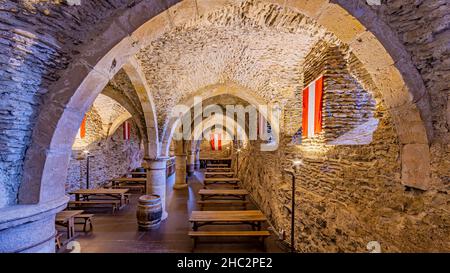 Vianden, Luxembourg.25 septembre 2021.Tables et bancs en bois entre les piliers, murs en pierre avec drapeaux illuminés à l'intérieur de la cave avec arche Banque D'Images