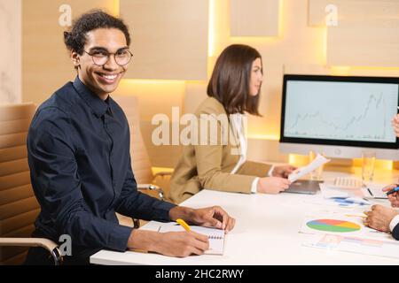 Écoutez attentivement.Un jeune homme d'affaires habile et agréable en chemise est assis à table et tient le stylo tandis que sa collègue responsable est assise à l'arrière-plan Banque D'Images