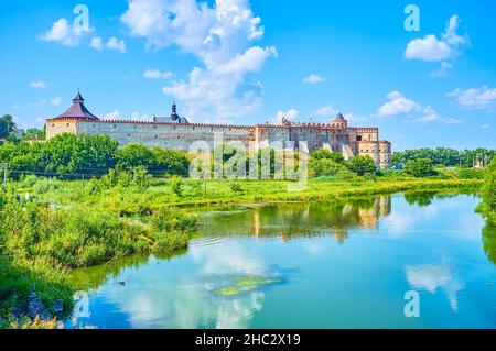 Le pittoresque château médiéval de Medzhybizh et son reflet dans les eaux bleu clair de la rivière Buh Sud, entouré de verdure luxuriante, Ukraine Banque D'Images