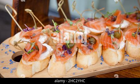 petits sandwiches avec fromage doux et saumon sur une table en bois.Apéritif à la baguette et au saumon Banque D'Images