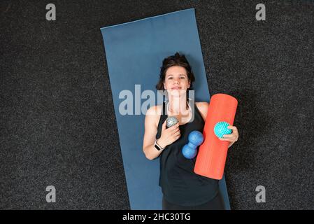 Jeune fille athlétique se trouve sur un tapis de yoga avec divers rouleaux myofascial.Equipement pour MFR.Version myofasciale.Vue de dessus. Banque D'Images