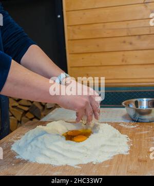 gros plan des mains de la femme pétriant la farine et les œufs sur une pâte à pâtisserie en bois Banque D'Images