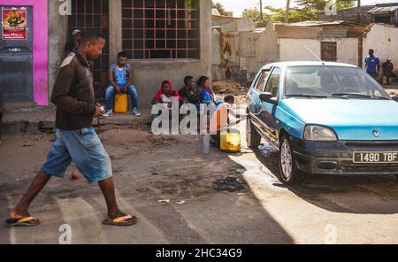 Ilakaka, Madagascar - 05 mai 2019: Groupe de malgaches inconnus assis sur un porche en pierre, homme nettoyant sa roue de voiture près, une autre personne marchant moi Banque D'Images