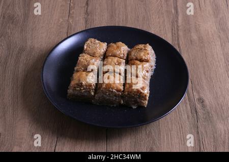 Baklava, dessert turc traditionnel nommé Baklava dans une assiette noire sur fond de bois.Accent sélectif sur le baklava central.Concept de Ramadan Banque D'Images