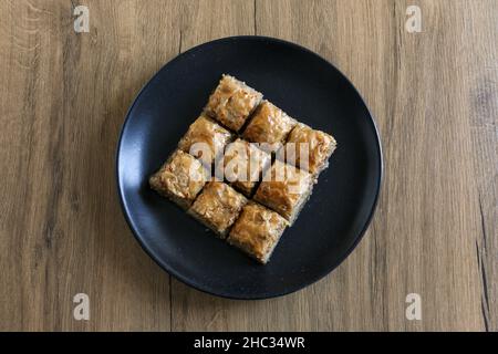 Baklava, dessert turc traditionnel nommé Baklava dans une assiette noire sur fond de bois.Accent sélectif sur le baklava central.Concept de Ramadan Banque D'Images